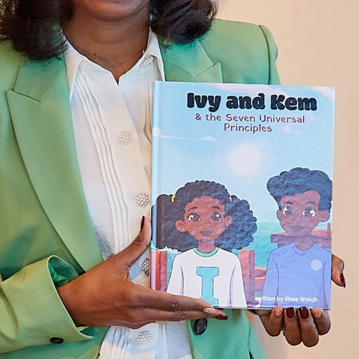 A person holds a children's book titled "Ivy and Kem & the Seven Universal Principles." 