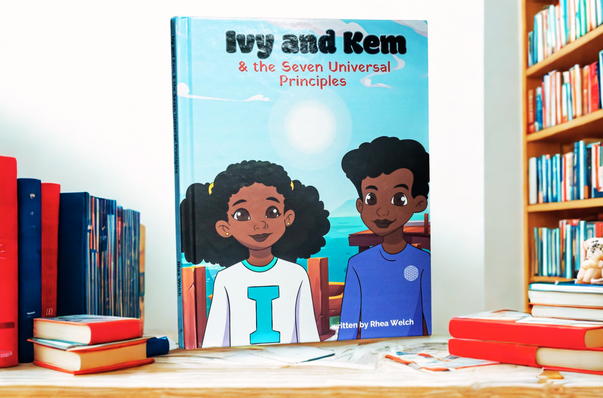 Children's book titled "Ivy and Kem & the Seven Universal Principles" standing upright on a wooden table, surrounded by books on a shelf and tabletop.