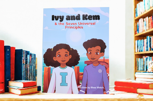 Children's book titled "Ivy and Kem & the Seven Universal Principles" standing upright on a wooden table, surrounded by books on a shelf and tabletop.
